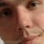Pixelated close-up of a person's face showing eyes, nose, and mouth with brown and pinkish skin tones, dark hair, and a neutral expression.