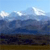 Pixelated landscape with blue sky, white clouds, and layered terrain in dark blue and brown hues.