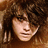 Pixelated close-up of a person with dark curly hair and light skin, wearing dark sunglasses, against a brown-toned background.