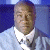 Pixelated image of a person in a light blue shirt with a white collar and dark tie against a blue background.