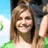 A static pixelated image shows a person with long brown hair smiling, wearing a green top against a blue sky background.