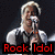 Pixelated image of a person with light hair holding a microphone, wearing a white shirt and dark vest against a dark background.