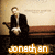 Pixelated image of a person in dark suit seated at desk with hands clasped, below text reading 'jonathan' on orange background.