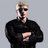Pixelated static image of a person with light hair, dark sunglasses, and a black shirt against a gray background.