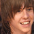 Pixelated close-up of a person with brown hair smiling broadly, showing teeth and tongue in a static image.
