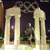 Pixelated image of two light-colored columns framing a dark background with indistinct figures and foliage.