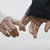 Two hands clasped together, one in a dark sleeve, against a light background with subtle pixelation.