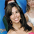 A static image shows a person with long dark hair smiling, wearing a green shoulder strap and a pink garment, against a blue background with partial figures.