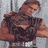Pixelated image of a person with brown hair wearing a dark sleeveless top and light-colored pants, standing against a gray background.
