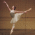 Pixelated static image of a ballerina in mid-pose with arms extended and one leg lifted, wearing a light-colored tutu against a brown background.