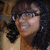 A person with dark curly hair and glasses smiles in a pixelated image with a light brown background.
