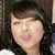 Pixelated close-up of a person with dark hair, light skin, and pink lips making a kissing face against a dark background.