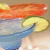 Pixelated image of a blue glass with yellow liquid and lemon slice, orange gradient background.