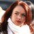 A pixelated close-up of a person with long reddish-brown hair wearing a white top against a blurred background.