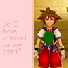 Pixelated character with spiky brown hair stands against a beige tiled background, wearing red pants and a white shirt with green and blue accents.