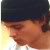 Pixelated close-up of a person's face with dark hair and a dark cap, showing partial facial features against a light background.