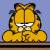 Pixelated yellow cat with brown stripes sits upright, mouth open in a wide grin showing white teeth against light blue background.