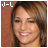 A pixelated image of a person with light brown hair and earrings, smiling against a solid reddish-brown background.