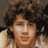 Pixelated close-up of a person with dark curly hair and light skin, wearing a white garment against a muted background.