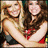 Two women in red and dark clothing embrace, one with long brown hair smiling broadly while the other has lighter hair and a neutral expression.
