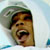 Pixelated static image of a person's face with green hair and brown skin tones, cropped to show only the upper portion against a light background.