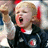 Pixelated image of a person with light hair wearing a dark suit, white shirt, and red tie, mouth open in a shout or yell.