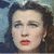Pixelated close-up of a person's face with dark hair, light skin, and red lips against a blue background.
