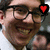 Pixelated close-up of a person with dark hair and glasses, wearing a light-colored shirt, with a red heart symbol in the top-right corner.