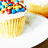A pixelated cupcake with white frosting and colorful sprinkles on a plate, viewed from above.