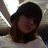 Pixelated static image of a person with dark hair and light skin wearing a white top against a blurred background.