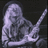 Pixelated grayscale image of a figure with long hair holding a guitar, seated in profile against dark background.