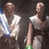 Two pixelated figures in a dark background, one with light hair and blue accents, the other bald with green accents, both wearing white tops and dark bottoms.