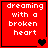 Red square icon with white pixelated text 'dreaming with a broken heart' and changing black or brown heart symbols at bottom right.