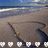 Pixelated beach scene with blue sky, ocean waves, and sandy shore, featuring a dark curved shape on the sand and white checkered patterns at the bottom.