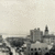 Pixelated grayscale cityscape with dark buildings against a light sky, no visible text or distinct characters.