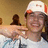A pixelated image shows a person wearing a white cap with red brim and dark hair, holding an object near their face against a brown background.