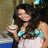 A woman with long dark hair wears a white dress with turquoise accents, holding a glass in one frame and bringing it to her mouth in another.