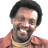 Pixelated image of a smiling person in an orange jacket and gold chain, with blue text reading "Happy Hour" and "OriginalIcons.com" on black backgrounds.