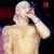 Pixelated image of a shirtless figure with light skin and short hair, standing against dark background with red and blue elements.