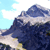 Pixelated mountain landscape with blue sky and white clouds, featuring dark blue peaks and light brown terrain under a bright sky.