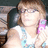 Pixelated image of a person with light brown hair wearing a white top with blue patterns and a pink accessory near the ear.