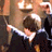 Pixelated static image of a character in dark clothing holding an object, with warm lighting and blurred background elements including what appears to be a candle or light fixture.