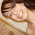 A woman with dark brown hair and light skin smiles broadly, showing teeth, in a close-up view with a light-colored background.