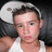 Pixelated image of a person wearing a white tank top and dark jacket, with short brown hair against a black background.