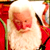Static 50x50 pixel icon of a cartoon Santa Claus with white beard and red suit, holding a green object against a blurred background.