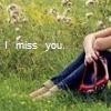 A person sits on grass with legs drawn up, wearing dark blue pants and a red-and-white striped item, with text reading "I miss you." overlaid.