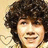 Pixelated close-up of a person with voluminous dark curly hair against a light beige background, showing partial facial features and a faint smile.
