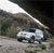 Pixelated image of a white vehicle on a road with a dark background and greenery on the left side.