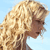 Pixelated profile of a person with light brown curly hair against a light blue background, showing side view of head and neck.