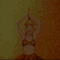 A woman in a gold and brown patterned bikini top and ornate headpiece raises her arms above her head against a gradient background shifting from green to orange.